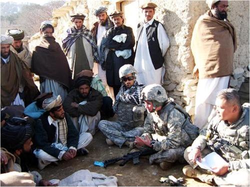 Field researchers seated in open ground with a gathering of village men during a community meeting
