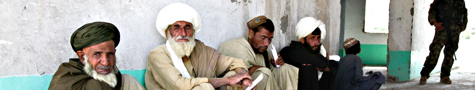 Village elders seated along a compound wall during a community gathering