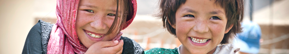 Two children smiling directly at the camera in a village setting