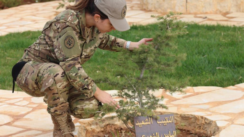 An officer tending a young tree planted at a memorial bearing an Arabic inscription