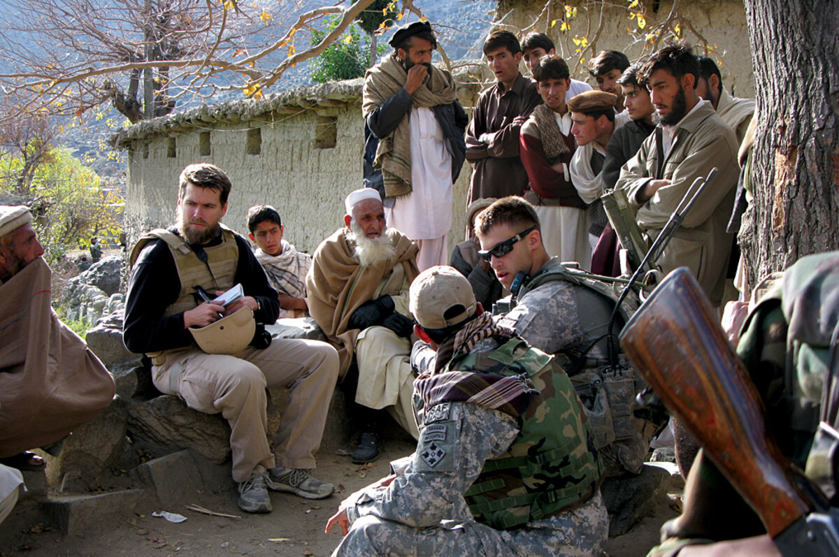 A civilian analyst taking notes among village elders and residents during a field shura